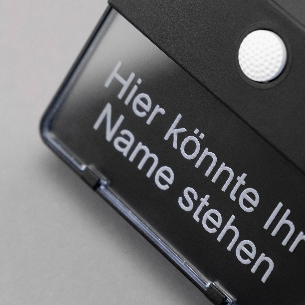 Schwarzer ETA 651-Klingeltaster auf grauem Hintergrund; auf dem Namensschild steht "Hier könnte Ihr Name stehen"